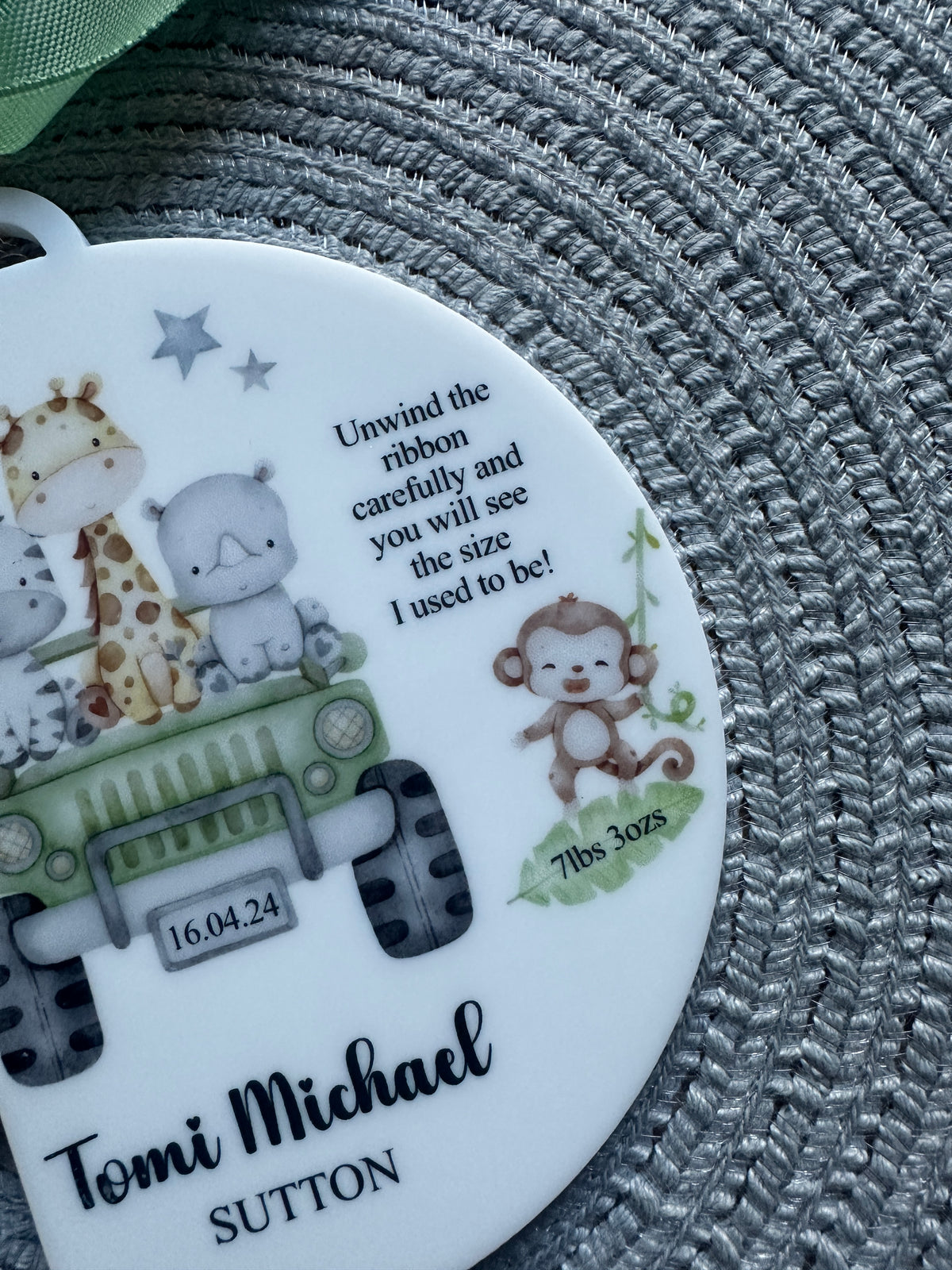 A close-up of a round white personalized keepsake or medallion featuring animal illustrations and the new baby's name and details.