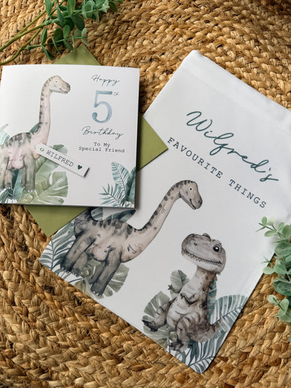 Dinosaur-themed birthday card and drawstring toy bag on a woven surface