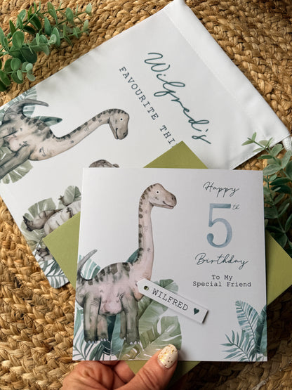 Dinosaur-themed birthday card with a hand holding it on a woven surface.