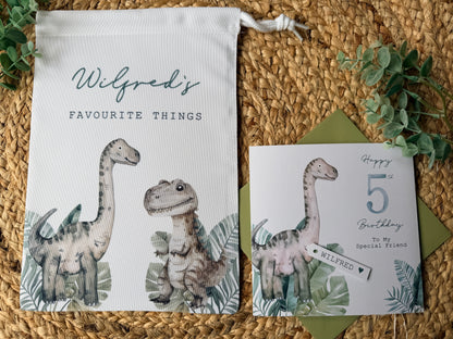 Dinosaur-themed toy bag and card on a woven surface with greenery.