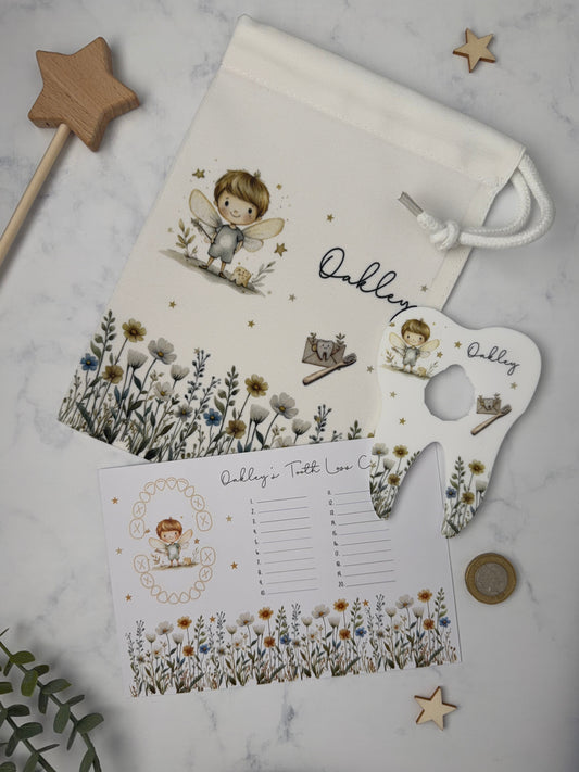 A white fabric tooth fairy bag with a matching printed tooth chart and acrylic shaped coin tooth holder, styled on a light marble surface with wooden star decorations and greenery.