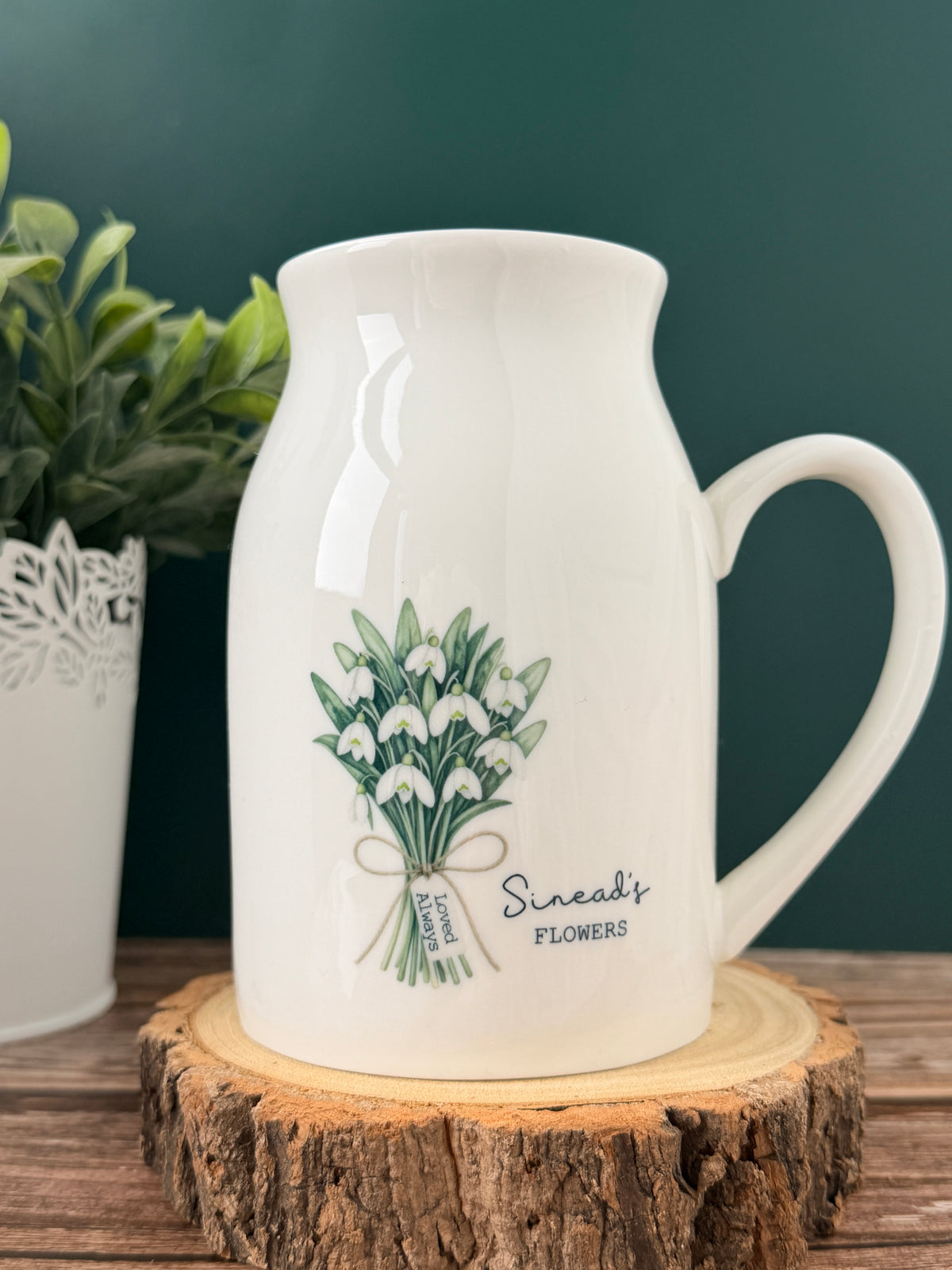 Personalised January birth flower jug featuring a watercolour snowdrop design, custom name and message tag, displayed on a wooden slice against a green background.