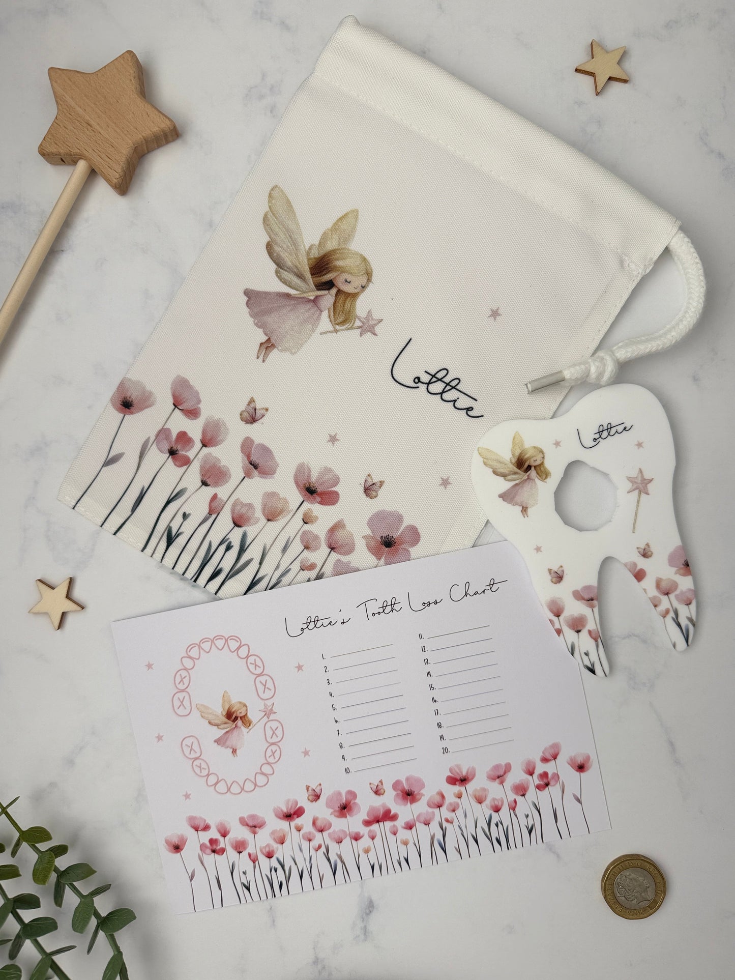 A styled flat-lay of a personalized fairy-themed letter set on a white marble background, including a drawstring pouch, a tooth loss chart and a coin holder.
