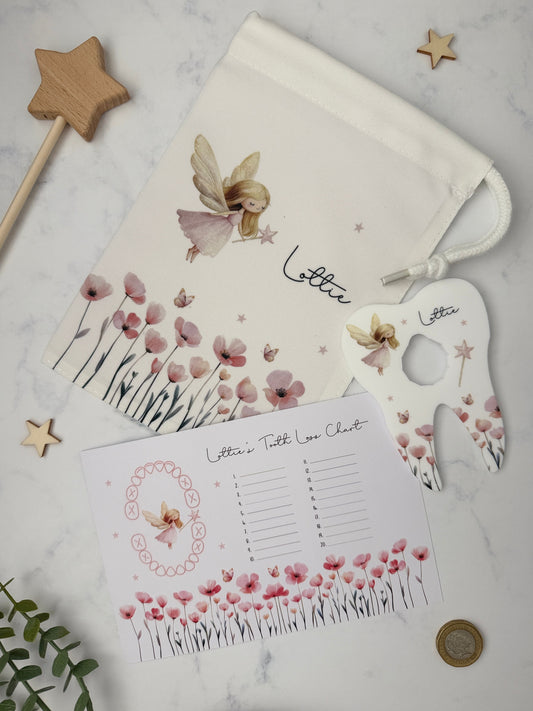A styled flat-lay of a personalized fairy-themed letter set on a white marble background, including a drawstring pouch, a tooth loss chart and a coin holder.