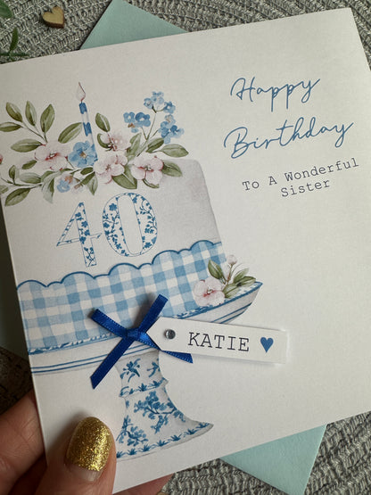 Birthday card with floral design and blue ribbon, held by a hand.