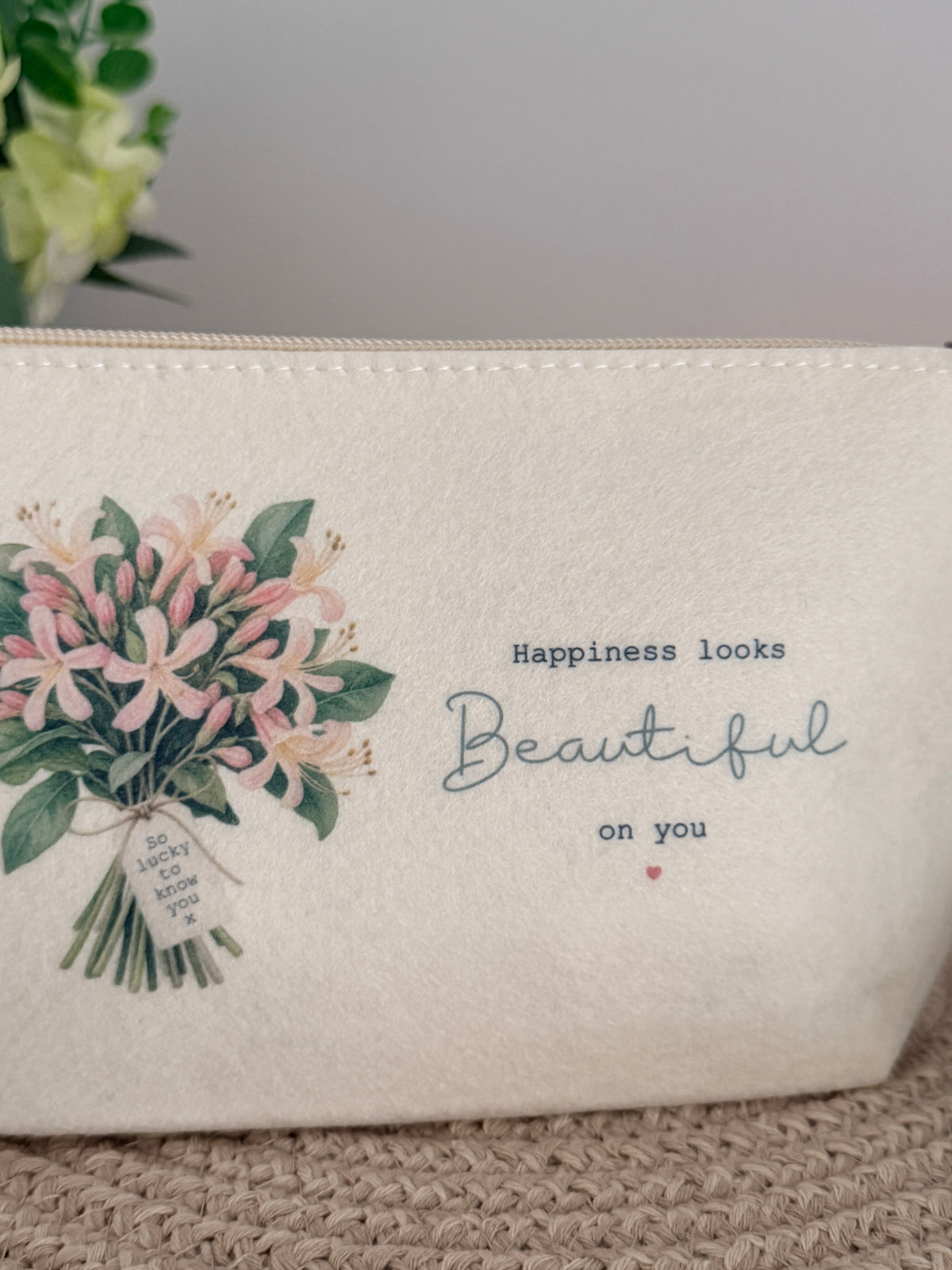 Personalised floral felt makeup bag styled on a neutral woven surface, a thoughtful gift for her.