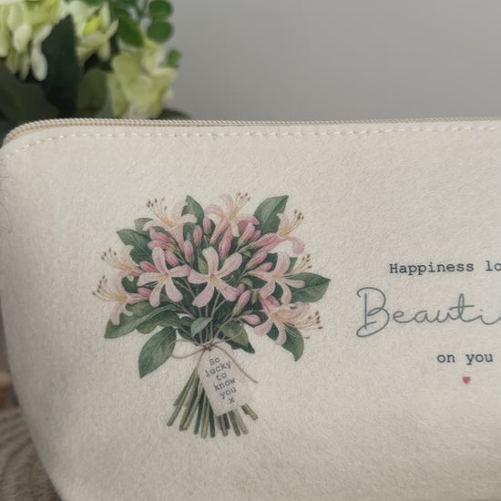 Personalised cream felt bag with floral bouquet artwork and uplifting wording, styled on a neutral woven surface.