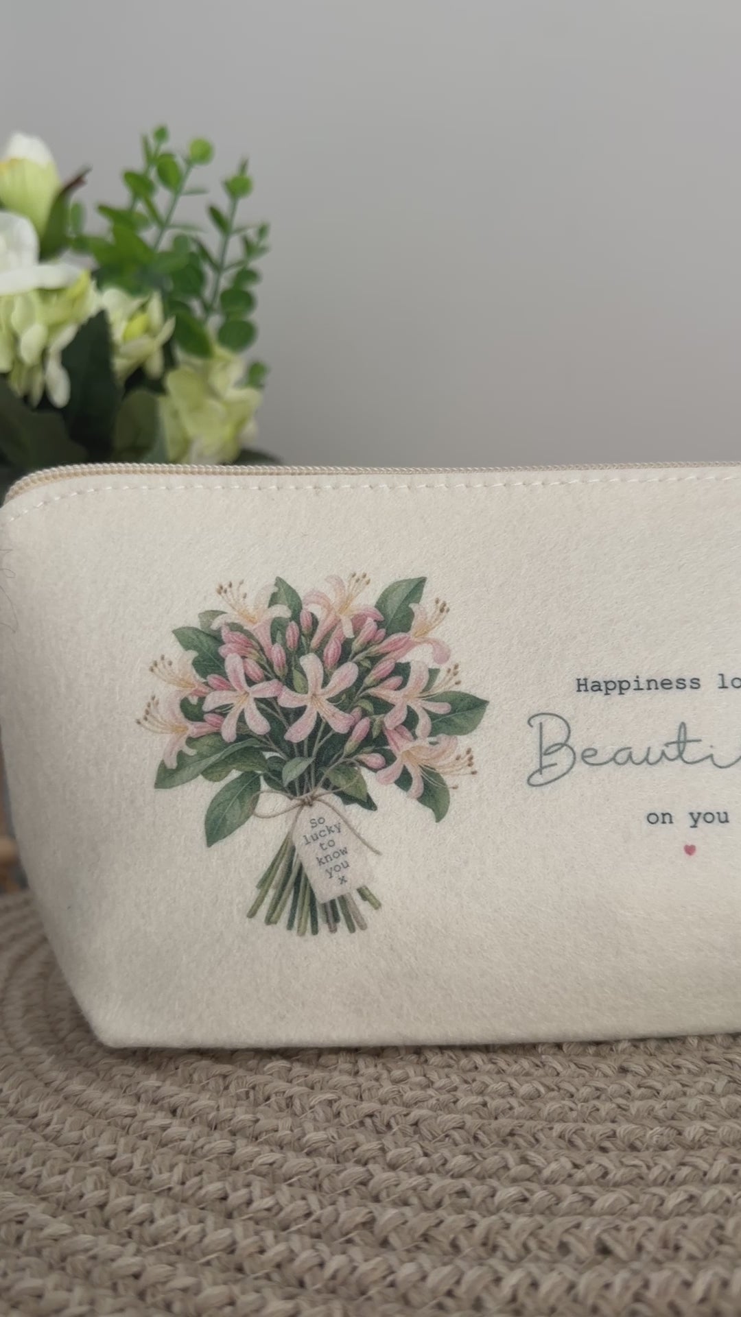 Personalised cream felt bag with floral bouquet artwork and uplifting wording, styled on a neutral woven surface.
